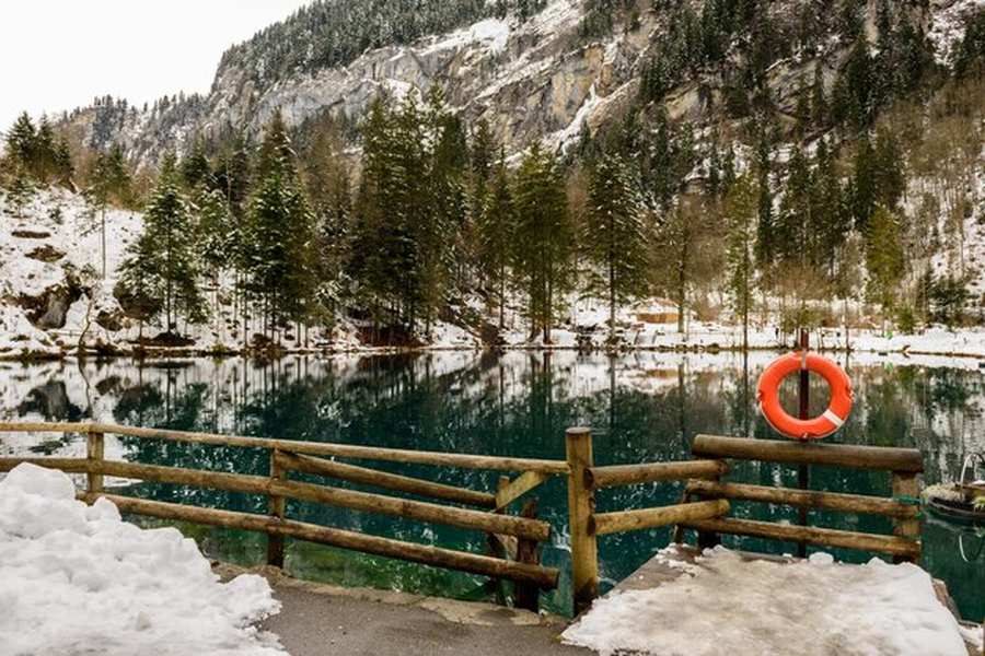 Un lac de montagne aux eaux cristallines entouré d'une forêt de conifères enneigée, illustrant parfaitement le concept de Coolcation : les meilleures destinations d'Europe du Nord pour fuir la canicule.