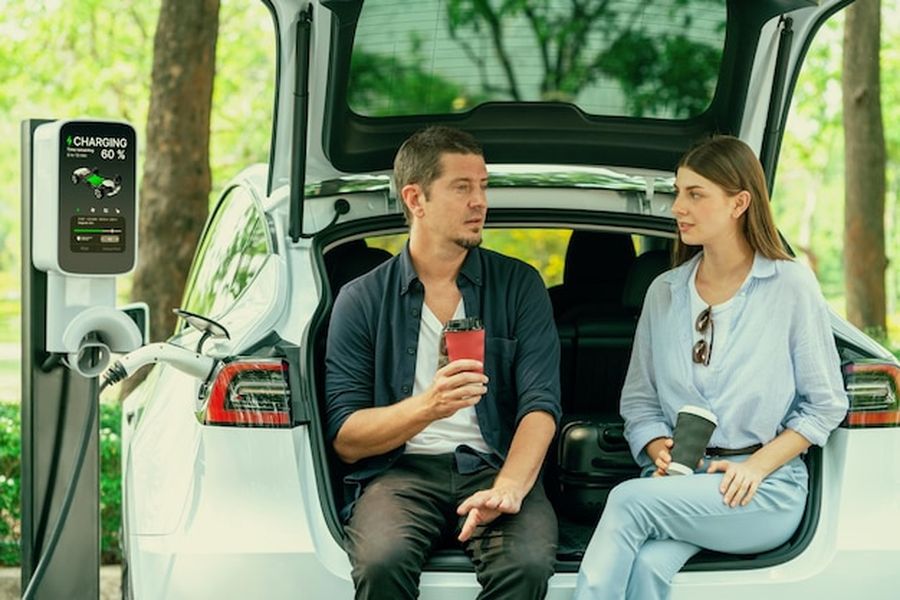 Un couple se détend avec un café pendant que leur véhicule charge, une étape clé de notre Guide pratique pour réussir un road trip longue distance en van électrique sans stress de recharge.