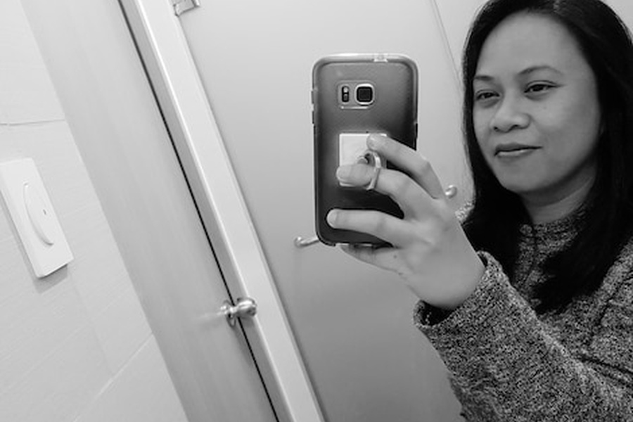 Une femme utilise son smartphone devant sa porte pour comprendre comment ouvrir une serrure connectée sans batterie et sans clé de secours.