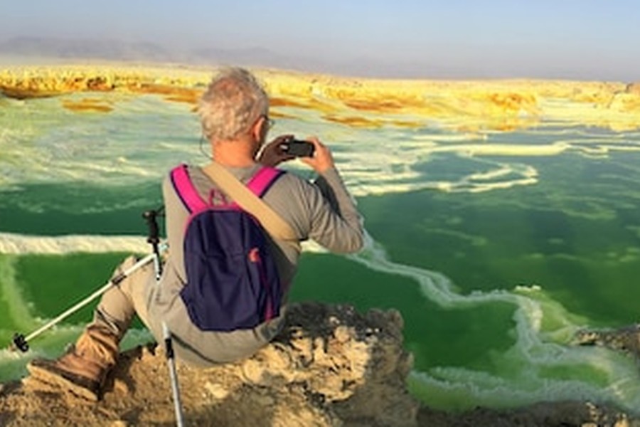 Un explorateur contemple un lac volcanique émeraude, illustrant le Tourisme de longévité : les meilleures destinations mondiales pour des retraites de régénération cellulaire.