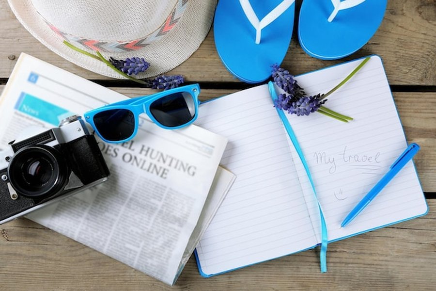 Accessoires de voyage, carnet de notes et appareil photo disposés sur du bois pour planifier des Destinations de 'Coolcation' : le guide pour choisir où voyager au frais durant l'été.