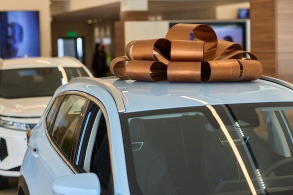 Une voiture électrique neuve bleu ciel ornée d'un grand nœud cadeau cuivré, prête pour la mise en place d'un Guide d'installation du Vehicle-to-Home (V2H) : utiliser sa voiture comme batterie domestique.