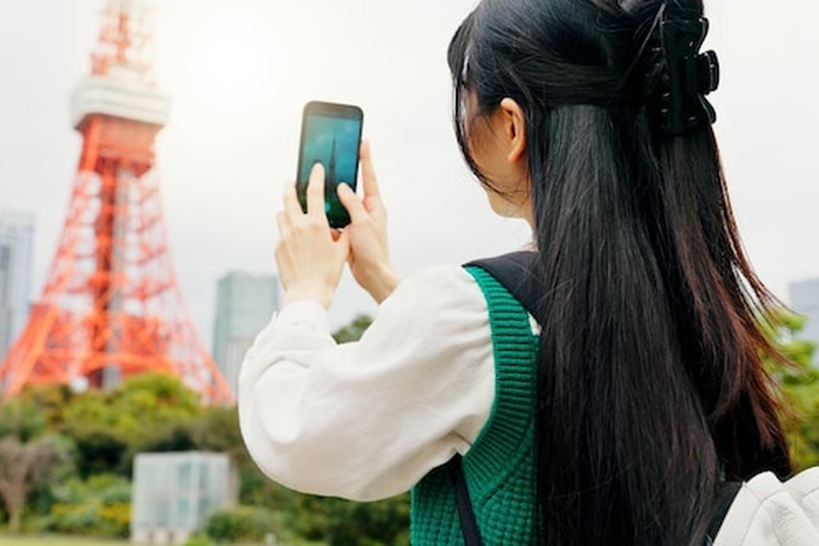 Une jeune femme photographie la Tokyo Tower avec son smartphone pour s'installer comme nomade digital au Japon : guide complet du visa et des meilleures villes d'accueil.