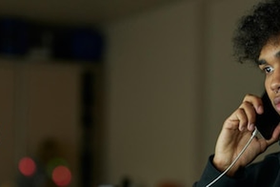 Un jeune homme attentif écoutant attentivement son smartphone pour apprendre comment reconnaître un appel frauduleux généré par IA.