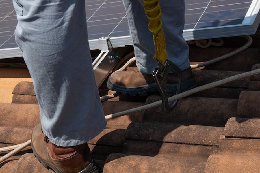 Technicien équipé d'un harnais de sécurité pour installer des tuiles solaires sur une charpente ancienne sans la renforcer sur une toiture en terre cuite.