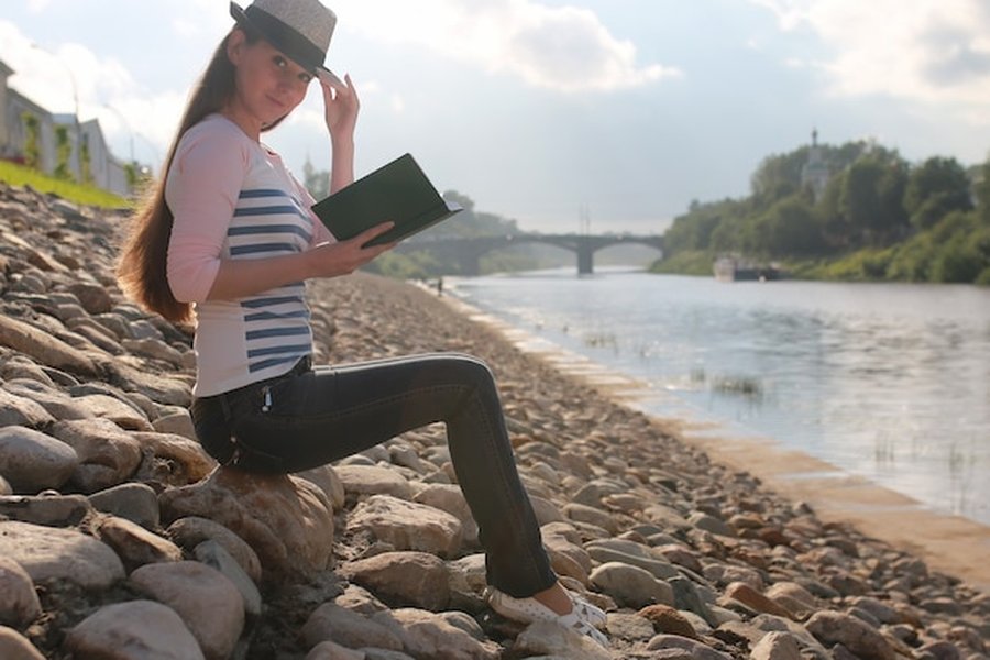 Une femme sereine lit un livre sur une berge rocheuse pour pratiquer le 'voyage silencieux' : les meilleurs sanctuaires pour déconnecter du bruit.