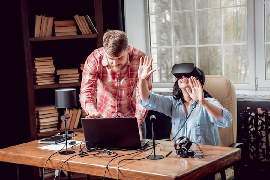 Un couple échange devant un ordinateur et un casque VR sur l'importance de savoir comment créer un code secret familial pour déjouer les arnaques au clone vocal.