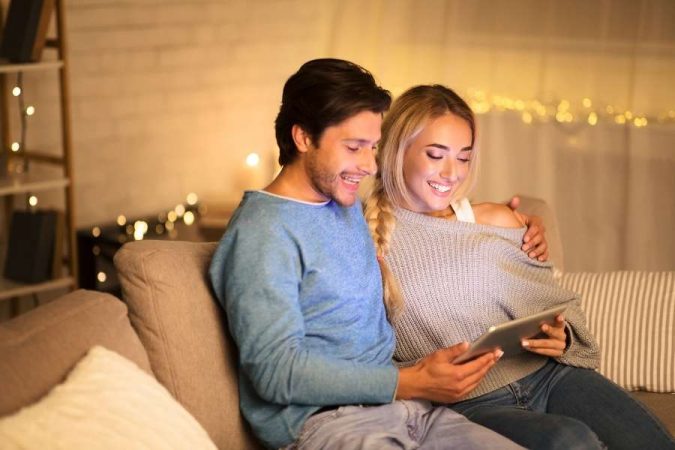 Une femme sourit en travaillant sur sa tablette numérique pour créer des visuels sur les réseaux sociaux.